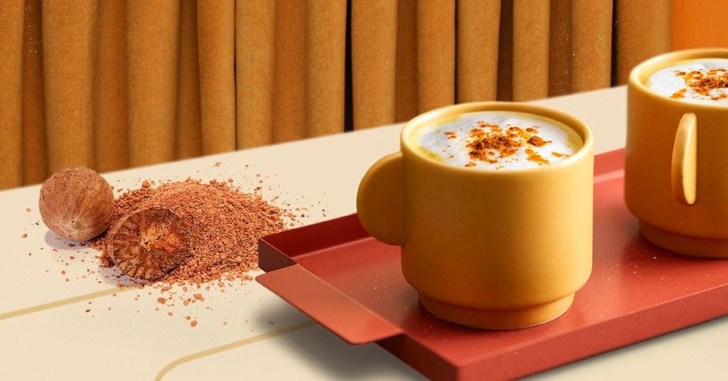 A small saucepan pouring golden-colored ashwagandha milk (moon milk) into a ceramic mug, with ingredients like ashwagandha powder and spices nearby